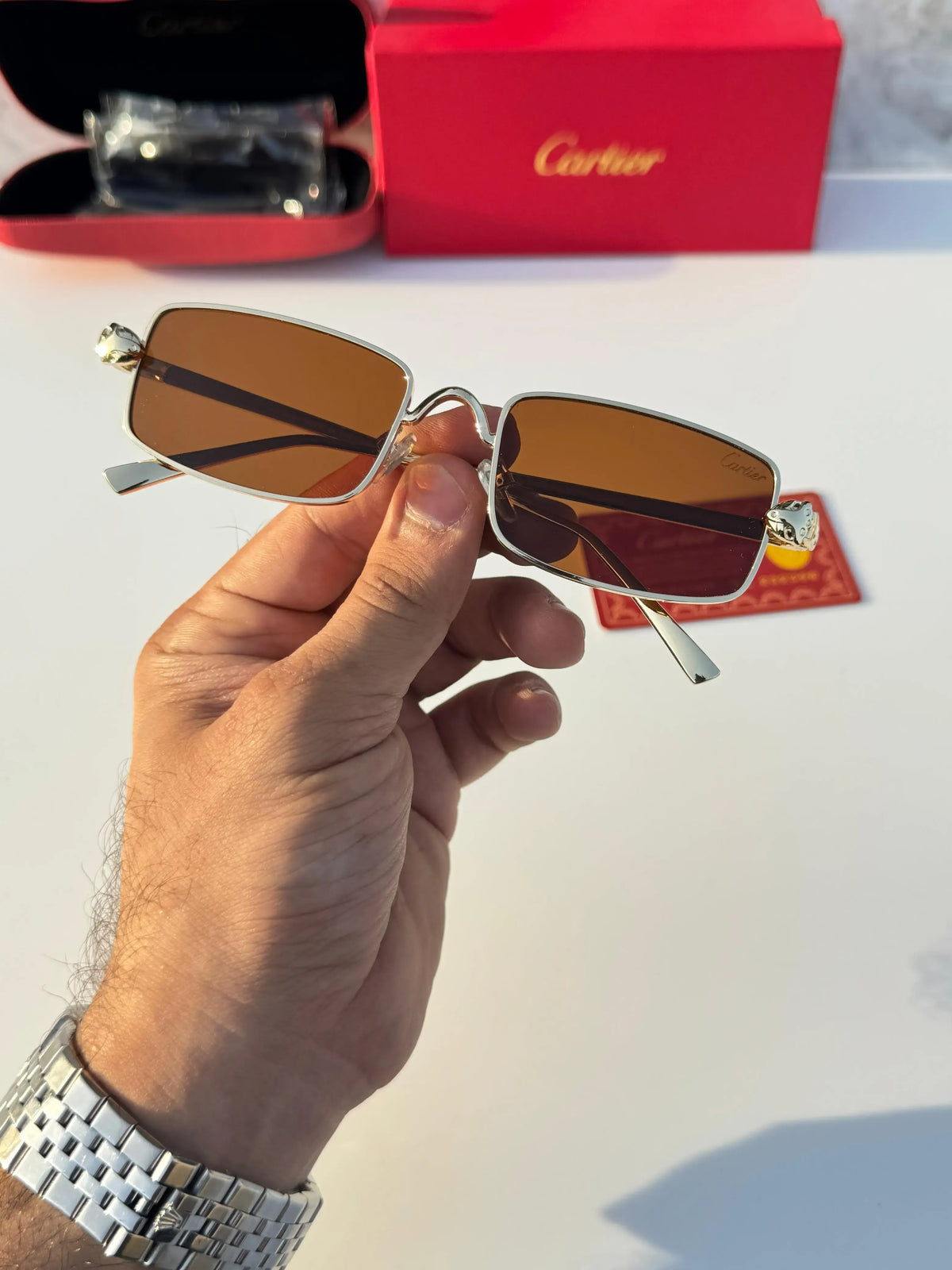 Gold rectangular sunglasses with brown lenses - held in hand showing full frame front view